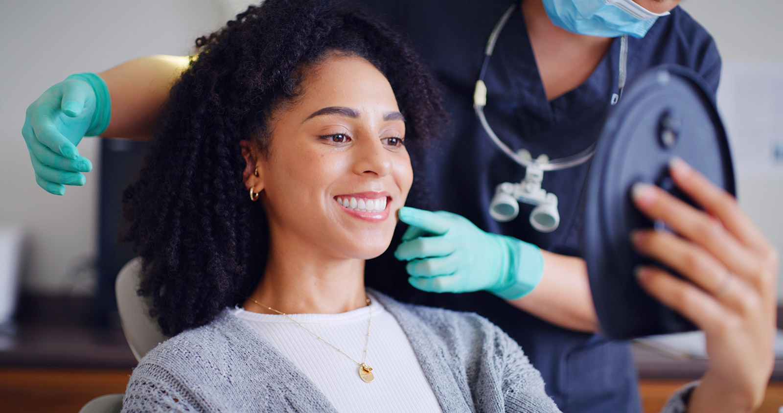 Patient smiling and reviewing her smile in a mirror with her dentist at Plaza Pointe Dental Specialists