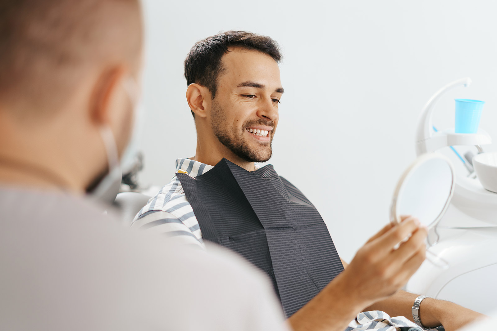 Smiling patient reviewing his smile in a mirror at Plaza Pointe Dental Specialists