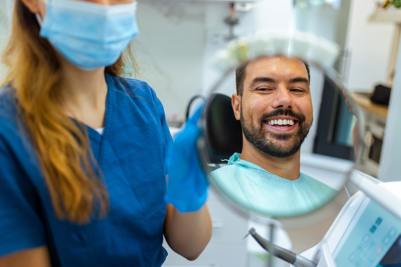 Smiling patient reviewing his teeth in a hand mirror with his dental hygienist at Plaza Pointe Dental Specialists