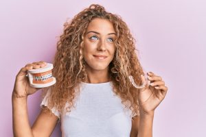 girl holding a clear aligner and model of teeth with braces